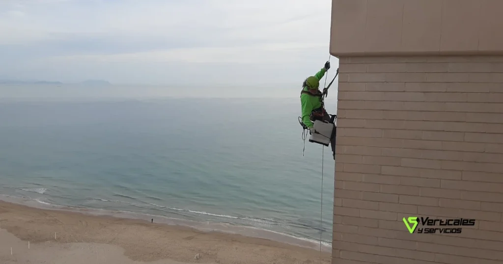 Operario de Verticales y Servicios sobre fachada vertical en un edificio junto a la playa.