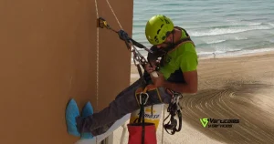 Operario de Verticales y Servicios mostrando el proceso para pintar la fachada sin andamios en un edificio junto al mar.
