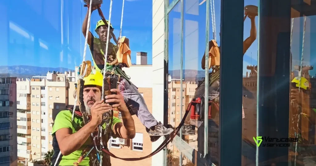 Trabajadores de Verticales y Servicios frente a un cristal de edificio en un servicio de limpieza de cristales en altura.
