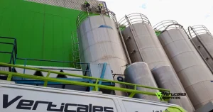Operarios de servicios verticales realizando tareas de mantenimiento y limpieza exterior en grandes silos industriales de metal.
