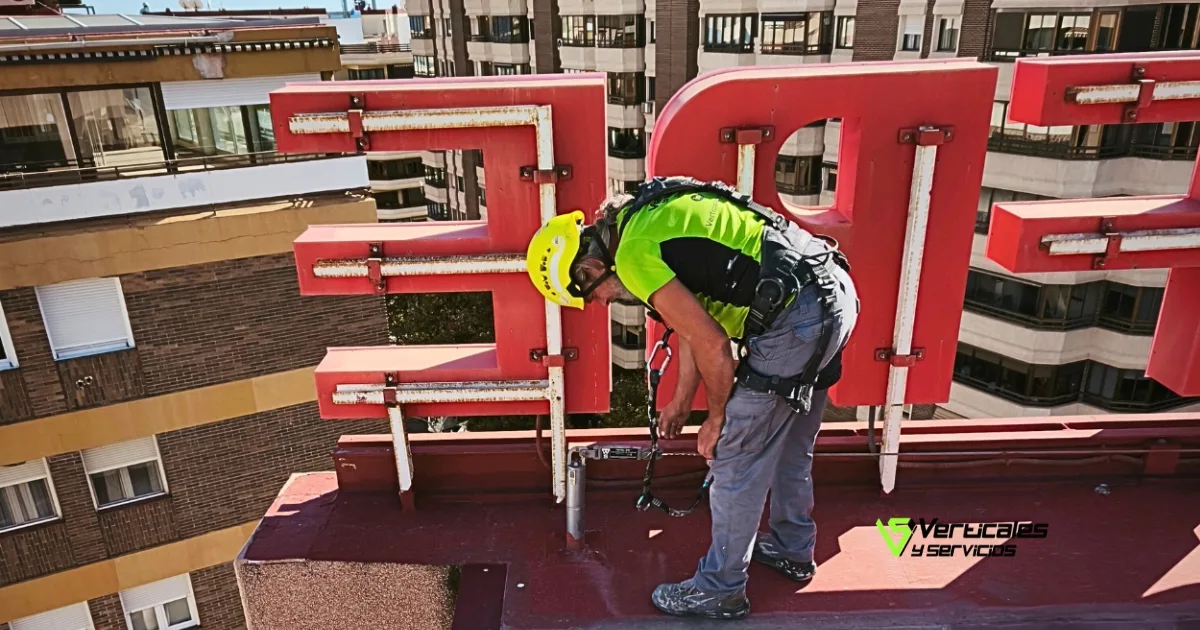 Técnico de servicios verticales instalando o revisando anclajes de seguridad en una azotea junto a un rótulo luminoso.